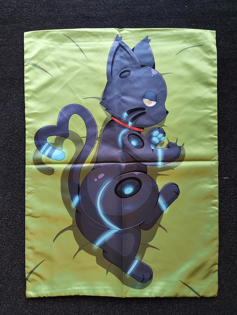 Puede incluir: Una funda de almohada rectangular con fondo verde claro y una ilustraci&oacute;n impresa de un gato estilizado de color gris oscuro. El gato tiene un collar rojo, marcas circulares de color azul brillante en el cuerpo y una cola en forma de coraz&oacute;n.