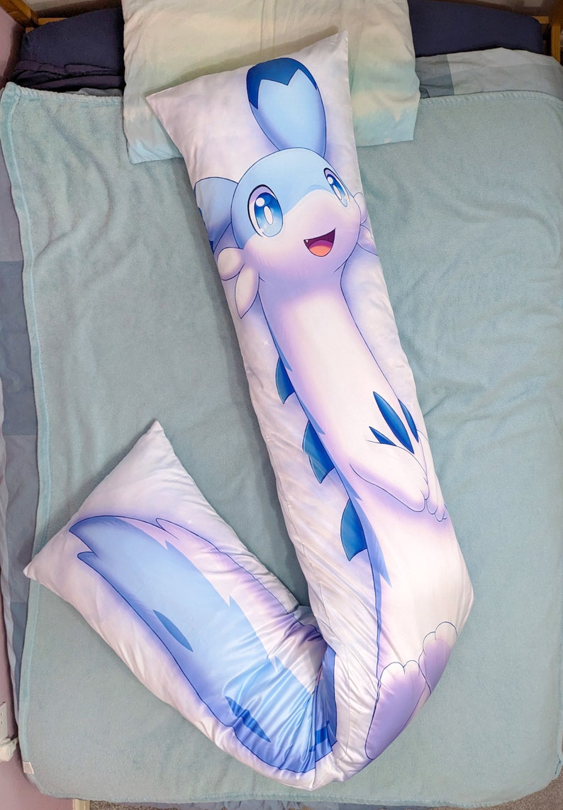 K&ouml;nnte beinhalten: Ein langes, wei&szlig;es Kissen mit einem blauen und wei&szlig;en Comic-Charakter darauf gedruckt. Der Charakter ist eine lange, schlanke Kreatur mit einem gro&szlig;en Kopf und einem langen Schwanz. Der Charakter hat einen blauen Kopf mit einem wei&szlig;en Gesicht und gro&szlig;en, blauen Augen. Der Charakter l&auml;chelt und hat einen kleinen, rosafarbenen Mund.