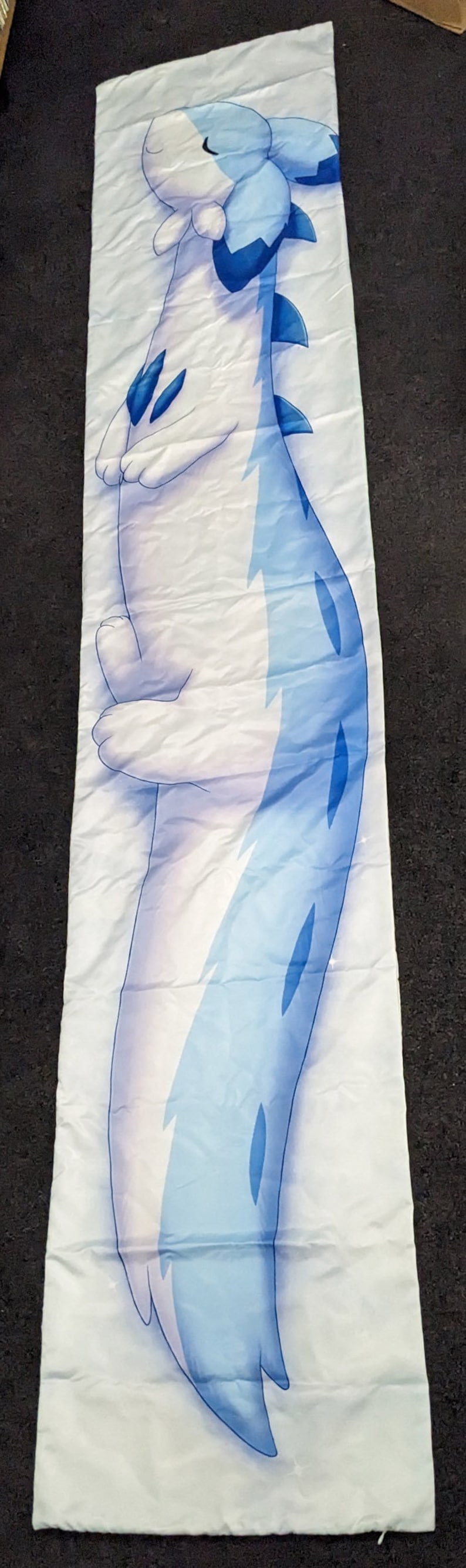 K&ouml;nnte beinhalten: Ein wei&szlig;-blaues Schlafkissen mit einem Cartoon-Drachen-Design. Der Drache ist zusammengerollt und hat die Augen geschlossen.