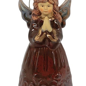 May include: A brown ceramic angel ornament with gold accents. The angel is wearing a long brown dress and has her hands clasped in prayer. She has long brown hair and a gold halo. The ornament has a gold string for hanging.