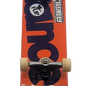 May include: A miniature skateboard with an orange deck featuring the word "FLIP" in a circle and the word "EXTREME". The skateboard has black trucks and tan wheels. A toy for skateboarding enthusiasts.