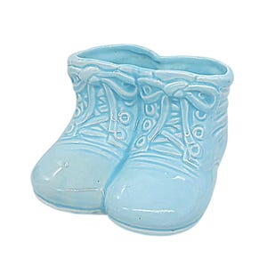 May include: A light blue ceramic planter shaped like a pair of baby shoes. The glossy finish highlights the molded details of the laces, eyelets, and stitching on the surface of the footwear. The top opening is hollow, providing space for small items.