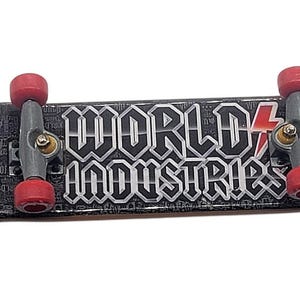May include: A black and gray finger skateboard with red wheels. The board features the text "WORLD INDUSTRIES" in white, with a red lightning bolt graphic. The board has a detailed graphic pattern.
