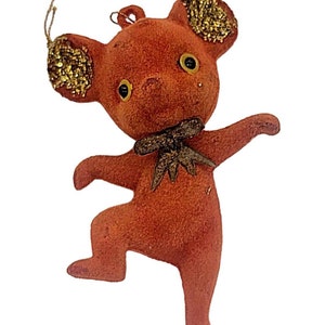 May include: A vintage brown felt teddy bear Christmas ornament with gold glitter ears and a brown bow. The bear has large yellow eyes and is standing on one leg.