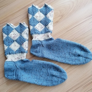 Könnte beinhalten: Ein Paar blaue und weiße gestrickte Socken mit einem Rautenmuster. Die Socken sind aus einem melierten Garn gefertigt.