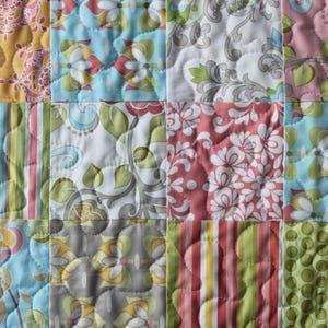 May include: A patchwork quilt with a variety of floral and geometric patterns in shades of pink, blue, green, and yellow.