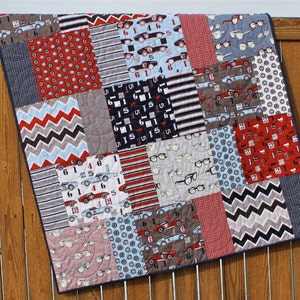 May include: A patchwork quilt with a variety of patterns, including red and blue cars, eyeglasses, and geometric designs. The quilt is made of cotton fabric and is quilted with a simple stitch.