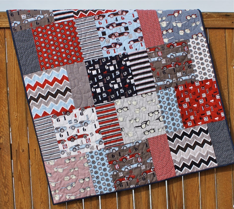 May include: A patchwork quilt with a variety of patterns, including red and blue cars, eyeglasses, and geometric designs. The quilt is made of cotton fabric and is quilted with a simple stitch.