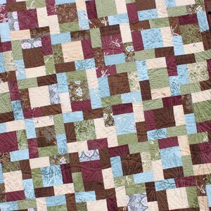 May include: A quilt made with a patchwork of squares in shades of brown, green, blue, and cream. The quilt is made with a variety of fabrics, including floral prints and geometric patterns.