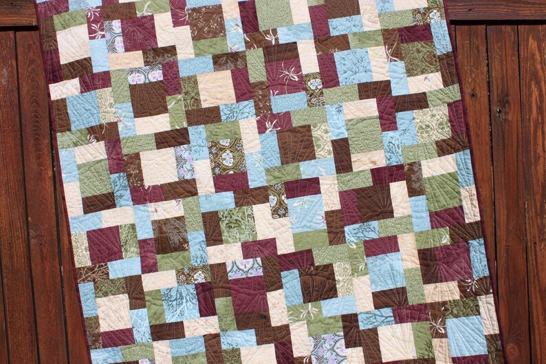 May include: A quilt made with a patchwork of squares in shades of brown, green, blue, and cream. The quilt is made with a variety of fabrics, including floral prints and geometric patterns.