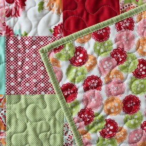 May include: A patchwork quilt featuring a range of colourful fabrics, including red, green, blue and pink. The quilt is made up of squares and rectangles, and the fabric is quilted in various patterns.