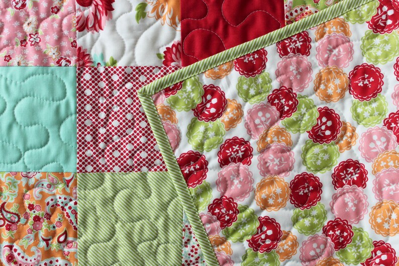 May include: A patchwork quilt featuring a range of colourful fabrics, including red, green, blue and pink. The quilt is made up of squares and rectangles, and the fabric is quilted in various patterns.