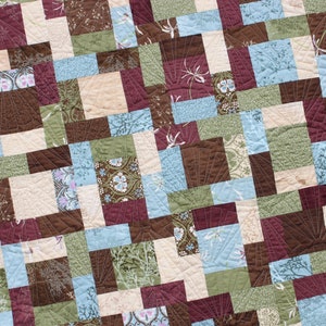 May include: A quilt made of various fabric squares in shades of brown, green, blue, and cream. The squares are arranged in a diagonal pattern, creating a geometric design.