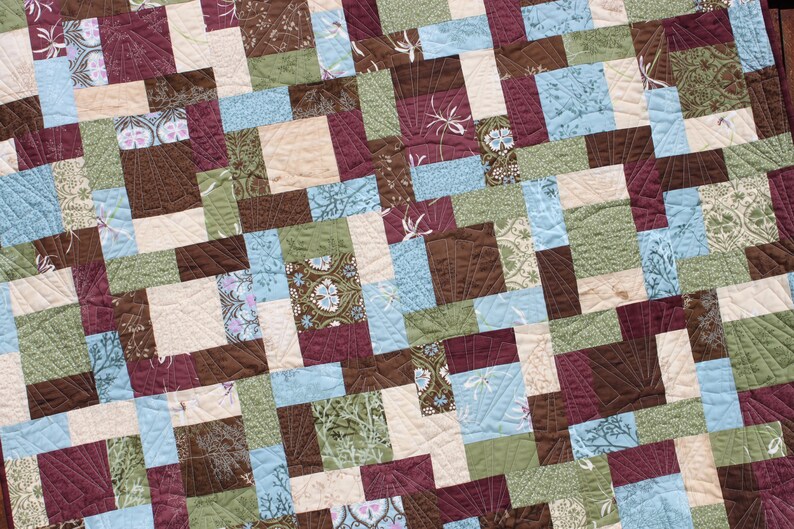 May include: A quilt made of various fabric squares in shades of brown, green, blue, and cream. The squares are arranged in a diagonal pattern, creating a geometric design.