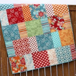 May include: A patchwork quilt with a variety of colorful fabrics, including red, orange, blue, green, and white. The quilt is made up of squares and rectangles, and the fabrics are arranged in a random pattern.