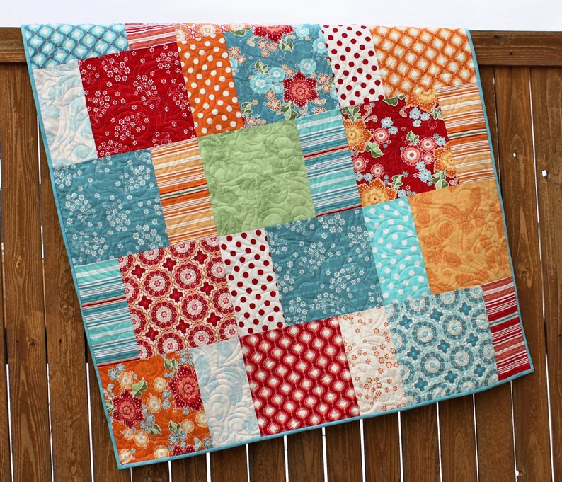May include: A patchwork quilt with a variety of colorful fabrics, including red, orange, blue, green, and white. The quilt is made up of squares and rectangles, and the fabrics are arranged in a random pattern.