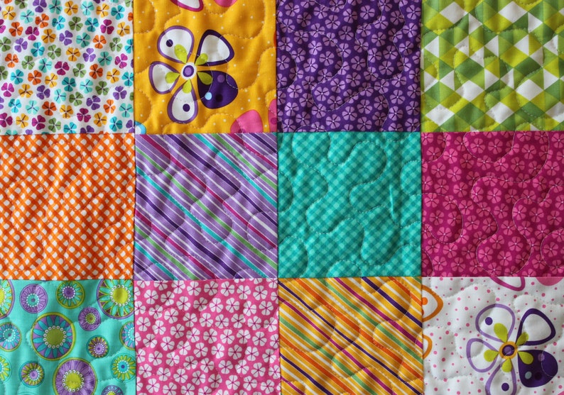 Pu&ograve; includere: Un quilt patchwork con quadrati di diversi colori e motivi, tra cui arancione, giallo, viola, rosa, verde e blu. Il quilt &egrave; realizzato in tessuto con motivi floreali, geometrici e a righe.
