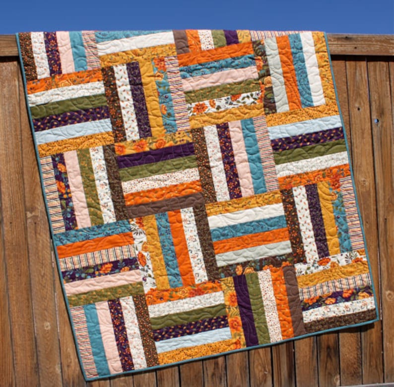 May include: A patchwork quilt with a variety of colorful fabric strips in shades of orange, brown, teal, purple, and white. The quilt is made with a simple pattern of horizontal and vertical strips, creating a geometric design.