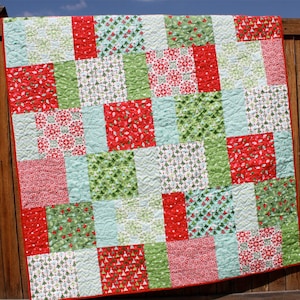 May include: A red, green, and white patchwork quilt with a variety of Christmas-themed patterns. The quilt is made of squares and rectangles, and it is quilted with a simple stitch.