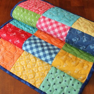 May include: A colorful patchwork table runner with a variety of patterns, including gingham, polka dots, and geometric designs. The runner is made of fabric and has a blue border.