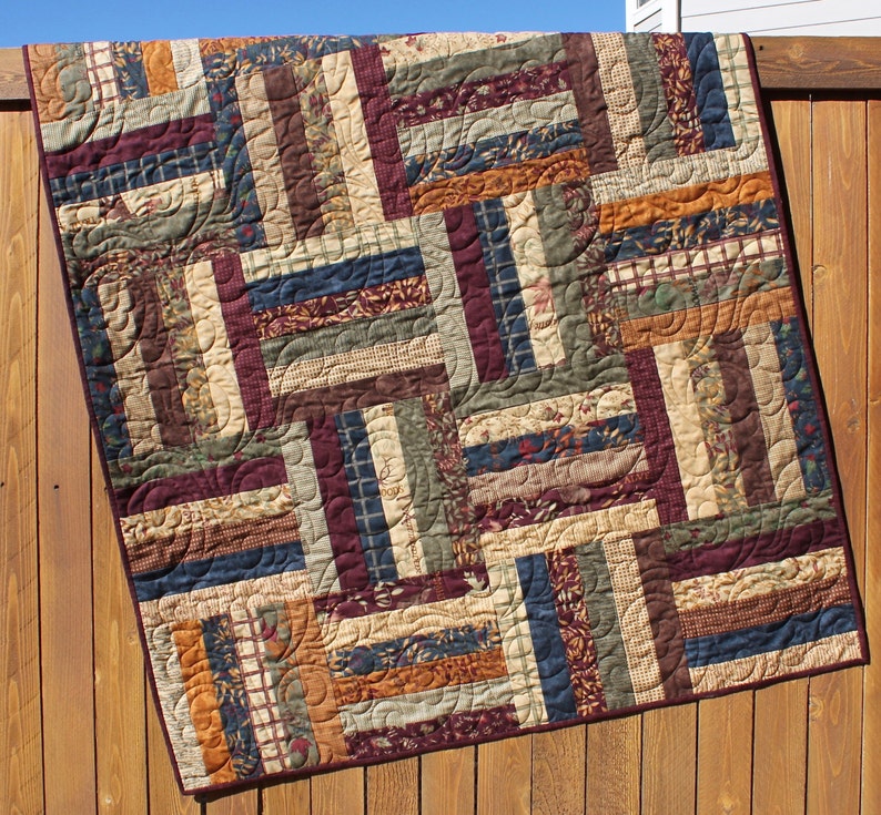 May include: A quilt made of various fabric scraps in shades of brown, green, blue, and orange. The quilt is made in a log cabin pattern with curved lines sewn into the fabric.