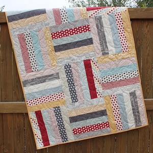 May include: A patchwork quilt with a variety of fabrics in shades of red, yellow, blue, and gray. The quilt is made up of strips of fabric sewn together in a random pattern. The quilt is edged with a yellow fabric.