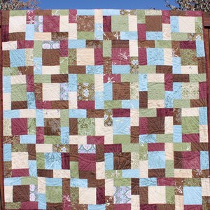 May include: A patchwork quilt with a variety of brown, green, blue, and cream squares. The quilt is made with different patterns and textures.