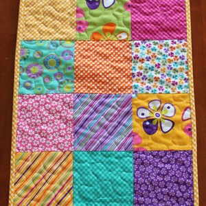 Pu&ograve; includere: Un runner da tavolo patchwork colorato con una variet&agrave; di motivi floreali e geometrici in tonalit&agrave; di giallo, verde, viola, rosa e arancione.