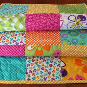 Pu&ograve; includere: Un runner da tavolo patchwork colorato con una variet&agrave; di motivi floreali e geometrici in tonalit&agrave; di rosa, verde, giallo, arancione e blu.