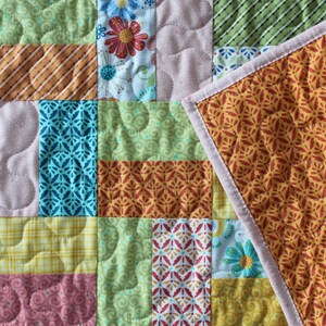 May include: A patchwork quilt with a variety of patterned fabric squares. The quilt features floral, striped, and geometric designs in shades of green, yellow, pink, and orange. The reverse side has a repeating floral pattern.
