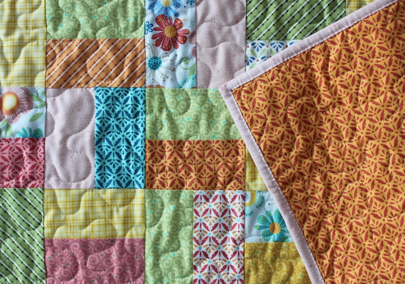 May include: A patchwork quilt with a variety of patterned fabric squares. The quilt features floral, striped, and geometric designs in shades of green, yellow, pink, and orange. The reverse side has a repeating floral pattern.
