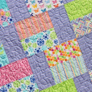 Op de afbeelding: Een kleurrijk patchwork-deken met verschillende patronen, waaronder vlinders, bloemen en geometrische ontwerpen. Het deken is gemaakt van verschillende stoffen in tinten roze, blauw, groen en geel.
