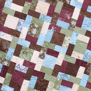 May include: A quilt made of various fabric squares in shades of brown, green, blue, and white. The squares are arranged in a diagonal pattern, creating a geometric design.