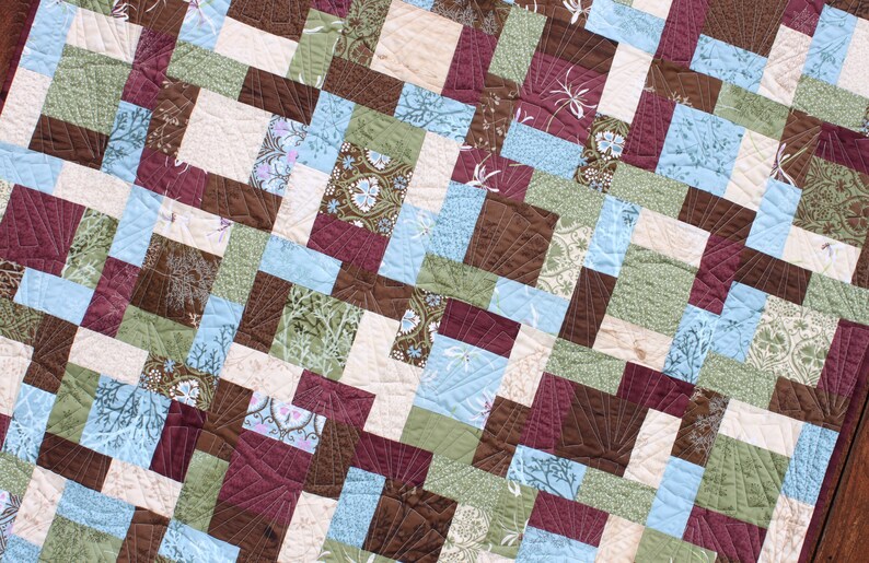 May include: A quilt made of various fabric squares in shades of brown, green, blue, and white. The squares are arranged in a diagonal pattern, creating a geometric design.