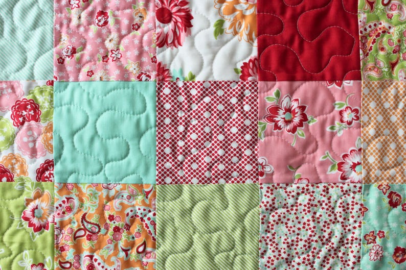 May include: A patchwork quilt featuring a range of floral patterns in shades of pink, red, green, and white. The quilt is made from different fabrics with various quilting stitches.