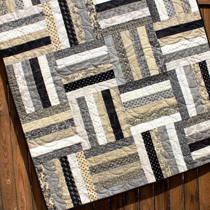 May include: A black and white quilt with a geometric pattern. The quilt is made of various fabrics with different textures and patterns. The quilt is quilted with a curved stitch.