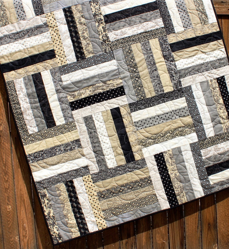 May include: A black and white quilt with a geometric pattern. The quilt is made of various fabrics with different textures and patterns. The quilt is quilted with a curved stitch.