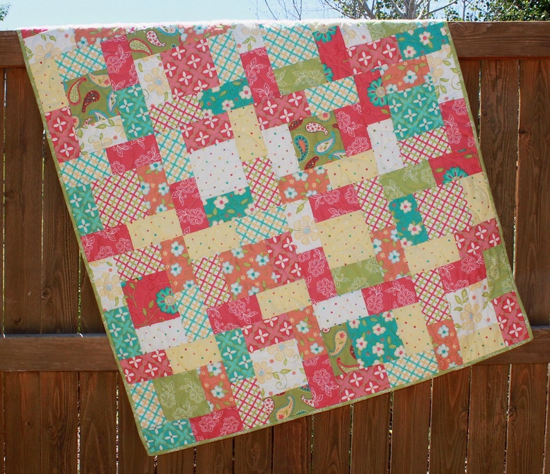 May include: A patchwork quilt with a variety of colorful squares in shades of pink, green, yellow, and blue. The quilt is made of cotton fabric and has a simple, modern design.