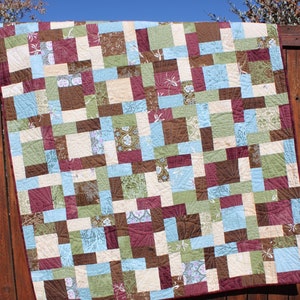 May include: A patchwork quilt with a variety of brown, green, blue, and cream squares. The quilt is made with different patterns and textures.