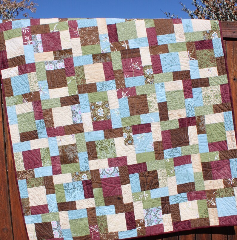 May include: A patchwork quilt with a variety of brown, green, blue, and cream squares. The quilt is made with different patterns and textures.