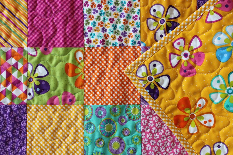 Pu&ograve; includere: Una trapunta colorata a patchwork con una variet&agrave; di motivi floreali e geometrici. La trapunta &egrave; realizzata con colori vivaci come giallo, arancione, rosa, verde e viola.
