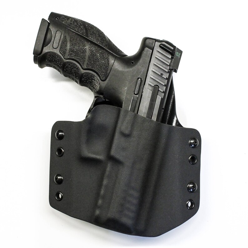 Puede incluir: Una funda de cuero negra con una pistola negra en su interior. La funda tiene varios botones a presi&oacute;n en el lateral.