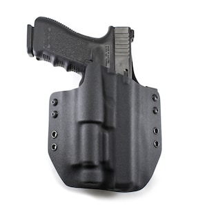May include: A black polymer holster with a black handgun inside. The holster has multiple screw holes and is designed for concealed carry.
