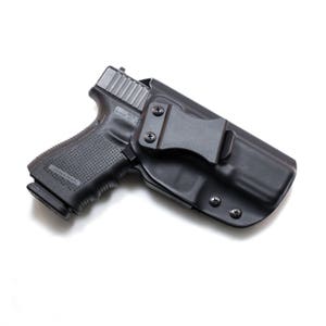 May include: A black handgun with a black holster and a clip. The holster has a metal clip that attaches to a belt.