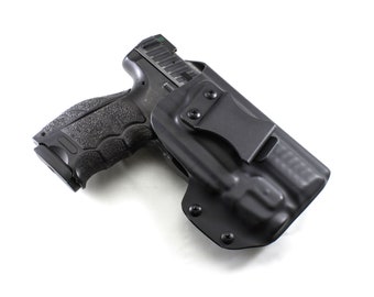 Puede incluir: Una pistola negra en una funda negra. La pistola tiene una empuñadura texturizada y una corredera plateada. La funda tiene un clip para el cinturón y está moldeada a la forma de la pistola. El fondo es blanco.