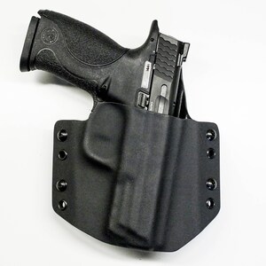 Puede incluir: Una funda de cuero negra con una pistola negra en su interior. La funda tiene varios botones a presi&oacute;n en el lateral.