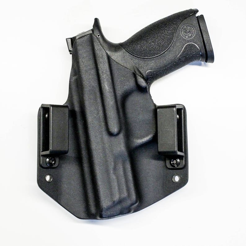 Puede incluir: Una funda de pol&iacute;mero negra con una pistola negra en su interior. La funda tiene dos clips ajustables a los lados.