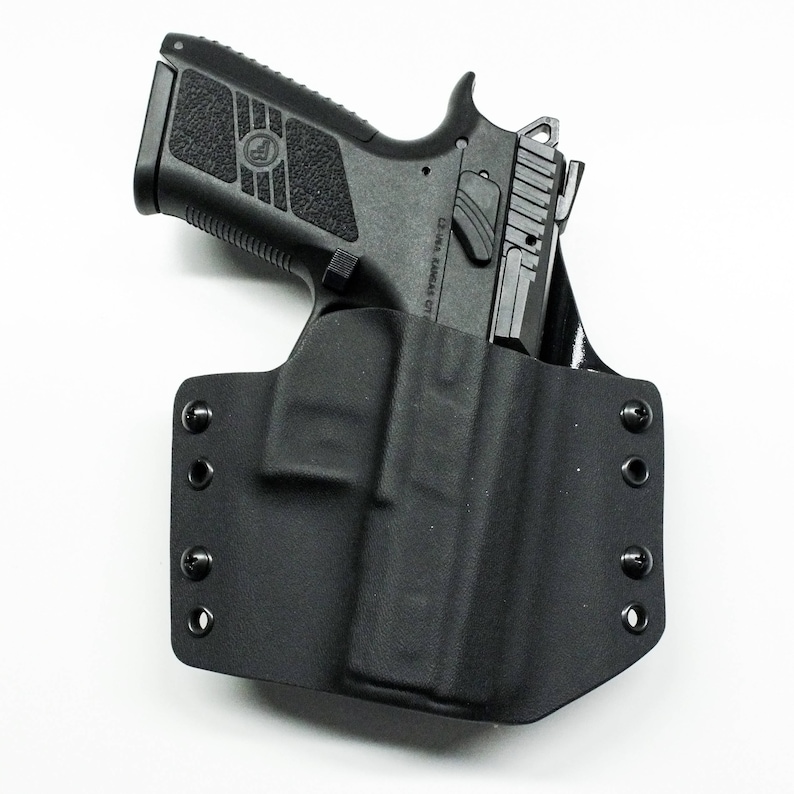 Puede incluir: Una funda de pistola negra con una pistola negra en su interior. La funda tiene varios botones a presi&oacute;n en el lateral.
