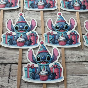 May include: Blue Stitch character wearing a party hat and holding a cupcake with a candle. Stitch is surrounded by presents and sitting on a white background. These are cupcake toppers.