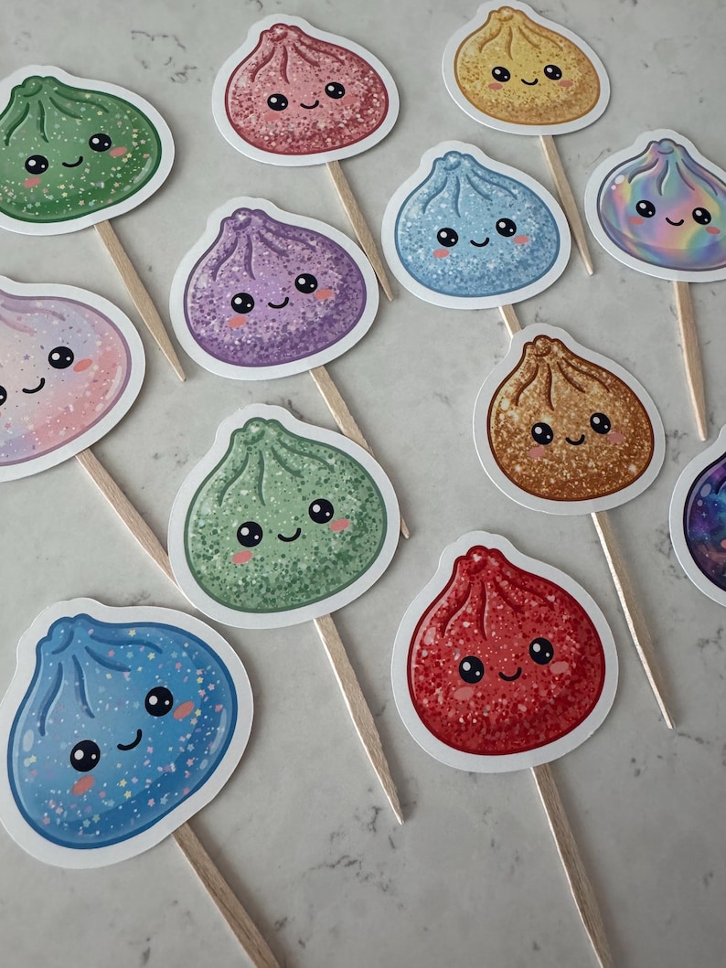 May include: A collection of cupcake toppers featuring various dumpling-shaped illustrations with smiling faces. Each topper is attached to a wooden pick and displays a unique color, including green, pink, yellow, blue, purple, and red, with glittery textures.
